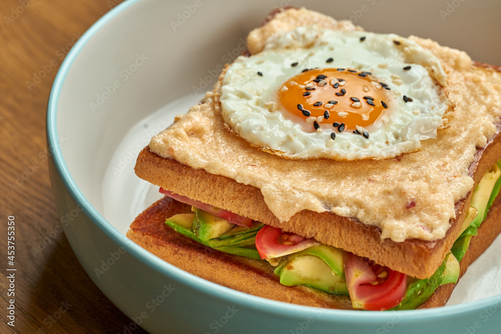 French sandwich Croque Madame with egg, cucumber, tomatoes, avocado and herring caviar in a plate on a wooden background