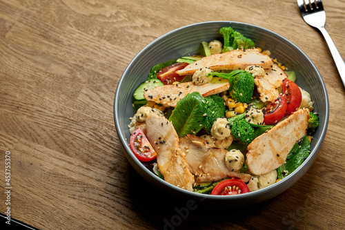 Diet salad with chicken, broccoli and cherry tomatoes in a bowl on a wooden background. Close up, selective focus with noise grain