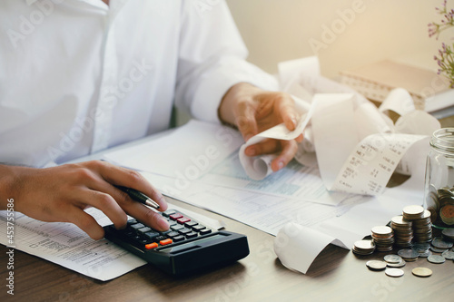 Man calculate domestic bills at home. Man using a calculator checking balance and costs at modern office.Business people doing paperwork for paying taxes.Expenses, account, taxes concept photo