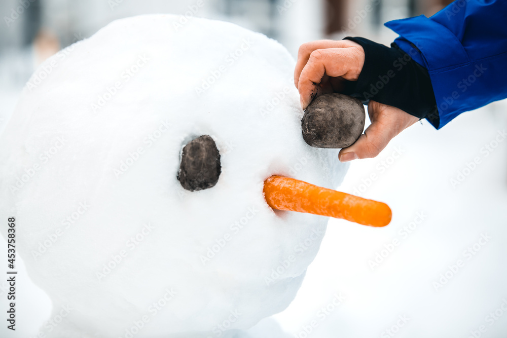 Man is decoration a snowman with stones and a carrot, funny winter activity