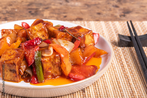 Spicy Korean vegetarian dish - sweet and sour tofu with onions and peppers on a bamboo napkin with chopsticks