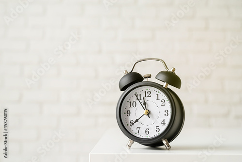 Black retro alarm clock on white brick wall background with copy space