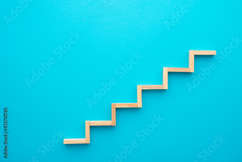 Flat lay of wooden blocks in shape of staircase step on blue background with copy space. Growth or development step by step for successful in business financial or education concept.