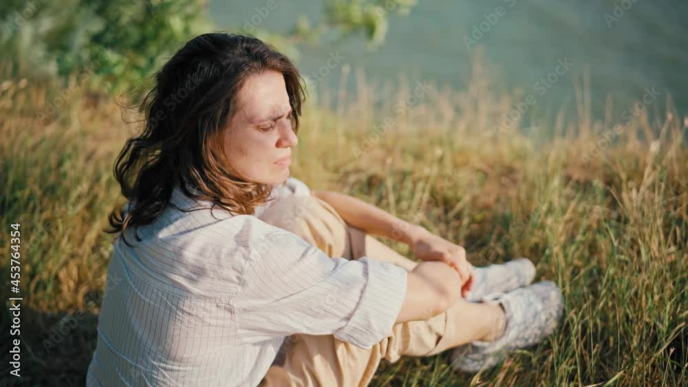 Handheld cinematic shot of a young woman sitting at the dry grass on the hill and looking to a view. The wind blows the female's hair and dry grass Handheld cinematic shot of a young woman sitting at the dry grass on the hill and looking to a view. The wind blows the female's hair and dry grass