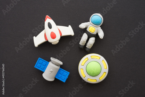 Flat lay of cute astronaut, rocket, satellite and ufo outer space eraser toy set on black background minimal style. Imagination, learning, back to school and education concept.
