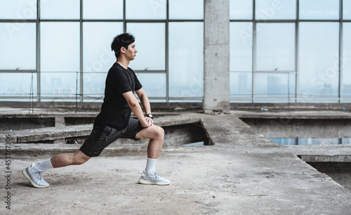 Young Asian man is doing leg stretching in an abandoned reinforced concrete building