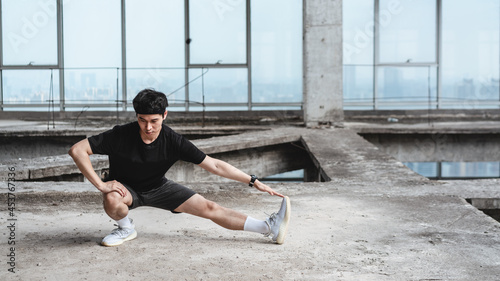 Young Asian man is doing leg stretching in an abandoned reinforced concrete building