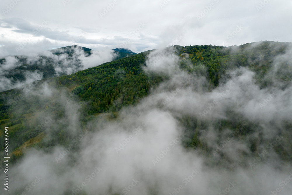 Rainy weather in mountains. Misty fog blowing over pine tree forest. Aerial footage of spruce forest trees on the mountain hills at misty day. Morning fog at beautiful summer forest.