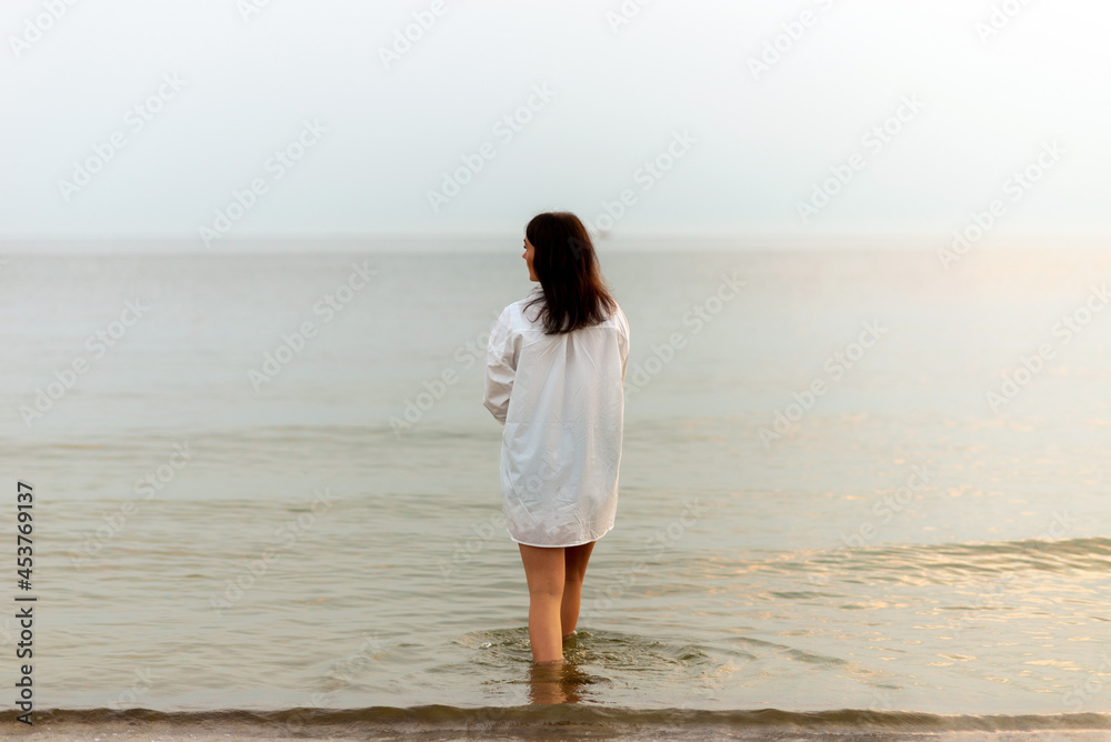 woman walking along beach and sea sunset background.Loneliness and sadness concept.Empty place for text.Back view.