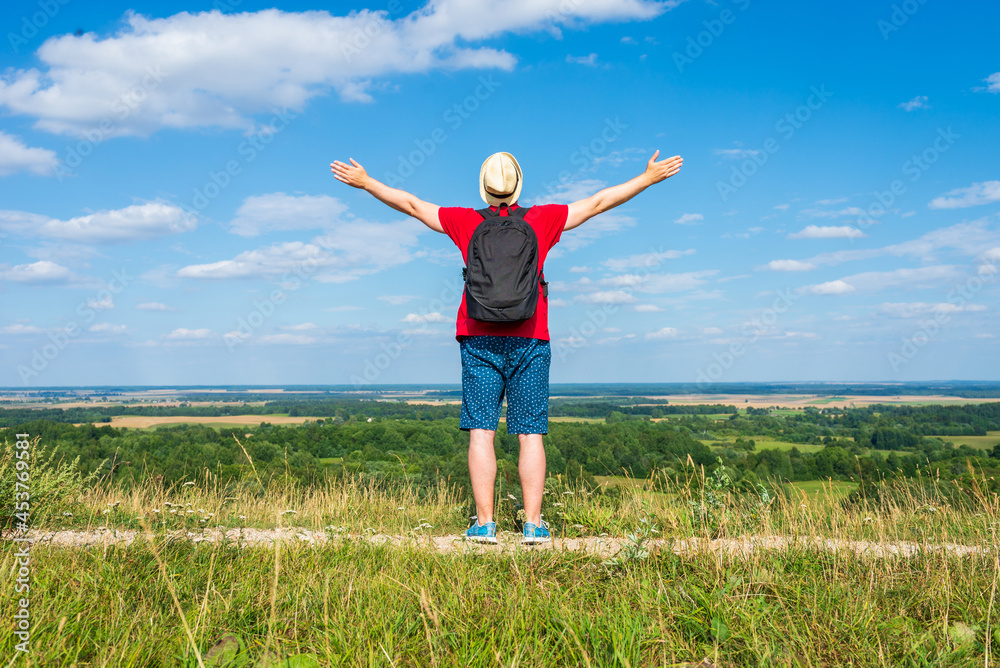 Tourist man with backpack enjoying the view in nature.Traveler man with backpack,arms outstretched stand on blue sky. Tourist man with backpack enjoying the view in nature.Traveler man with backpack,arms outstretched stand on blue sky.