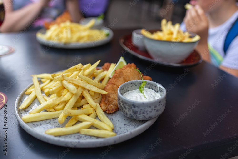 Lunch from fish in breadcrumbs and dough, french fries potatoes,Tartar sauce for fish. Outdoors blurred background. Lunch from fish in breadcrumbs and dough, french fries potatoes,Tartar sauce for fish. Outdoors blurred background.
