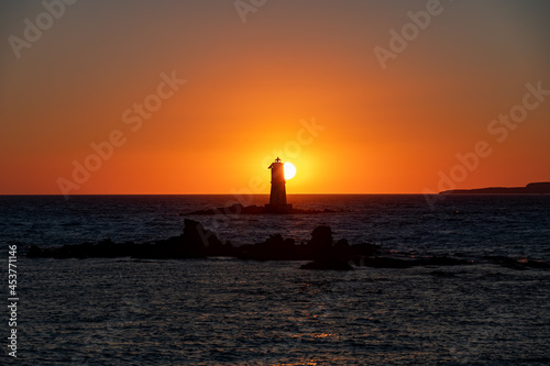The Sun is setting down behind the Mangiabarche's Lighthouse in front of Carloforte, Island of San Pietro, and Calasetta, Sant'Antioco