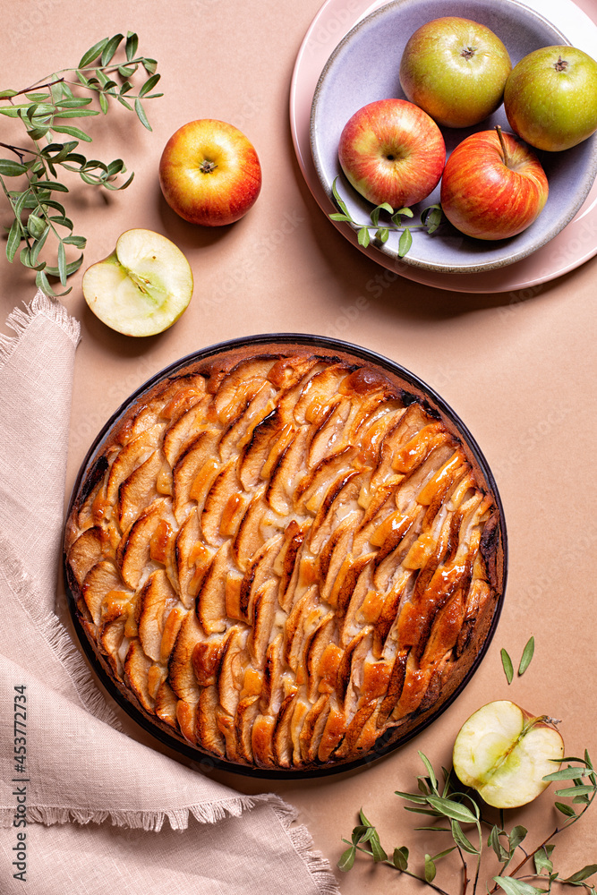 Apple pie decorated with apple slices and glazed. Fresh apple fruits, on a peach background. Copy space, vertical image. Apple pie decorated with apple slices and glazed. Fresh apple fruits, on a peach background. Copy space, vertical image.