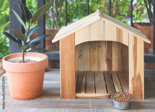 wooden dog's house with dog food bowl  in balcony decorated with houseplant in plant pot.