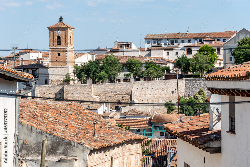 View of small town with church and picturesque houses with plastered facade and ceramic tile roofs on a sunny day. Chinchon, Madrid, Spain