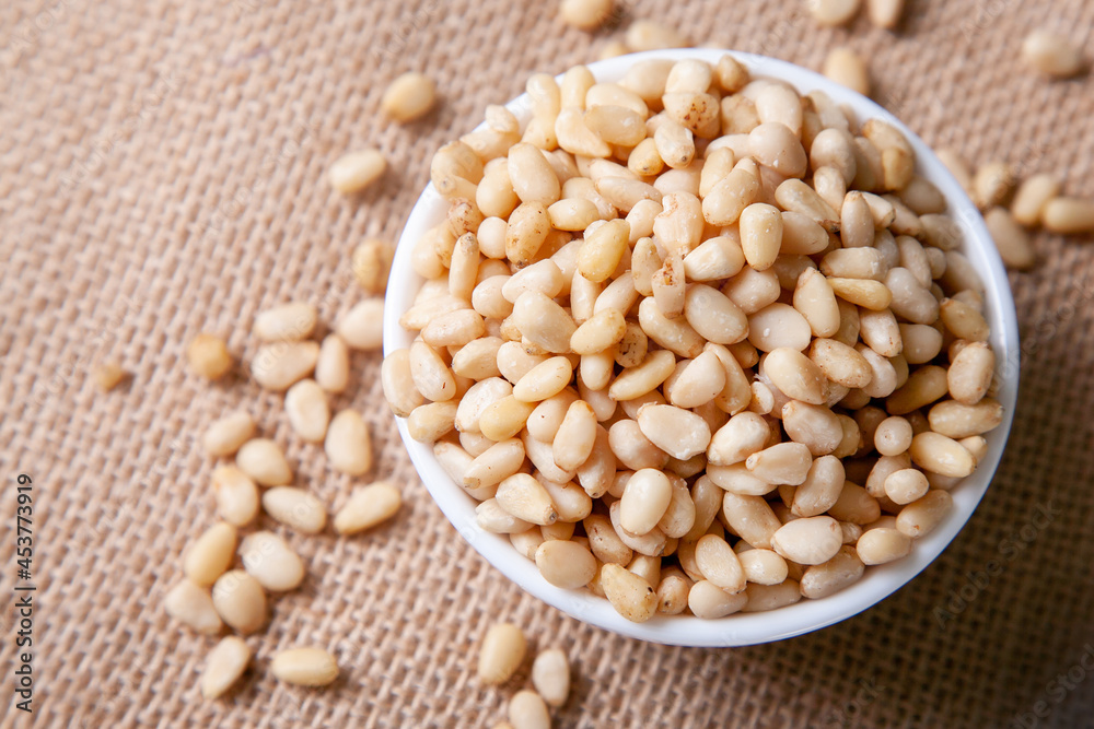 Fototapeta premium Organic Pine nuts in a bowl on a jute napkin top view flat lay