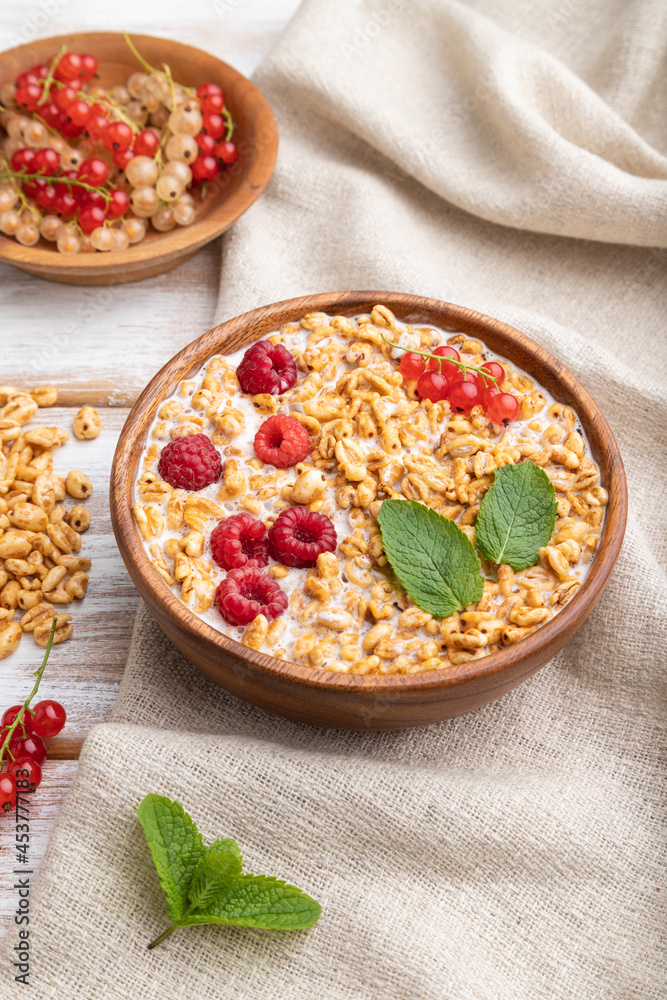 Wheat flakes porridge with milk, raspberry and currant in wooden bowl on white wooden background. Side view, close up. Wheat flakes porridge with milk, raspberry and currant in wooden bowl on white wooden background. Side view, close up.