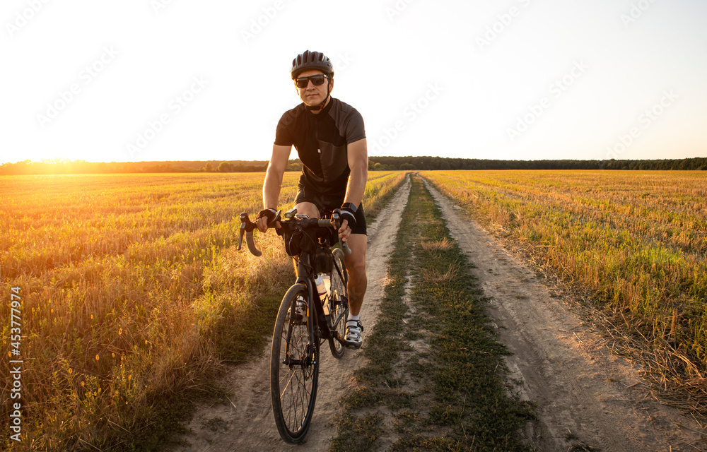 Bike traveler riding through the field at sunset on bicycle with bags