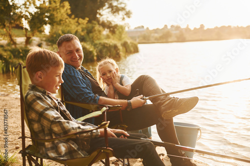 Sitting together. Father with son and daughter on fishing outdoors at summertime