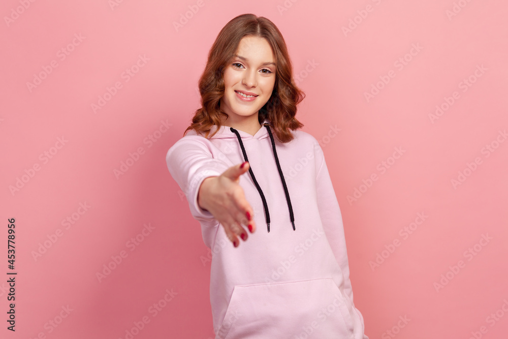Portrait of friendly smiling young female in hoodie stretching her hand welcoming guests, hospitality, nice to meet you sign. Indoor studio shot isolated on pink background Portrait of friendly smiling young female in hoodie stretching her hand welcoming guests, hospitality, nice to meet you sign. Indoor studio shot isolated on pink background