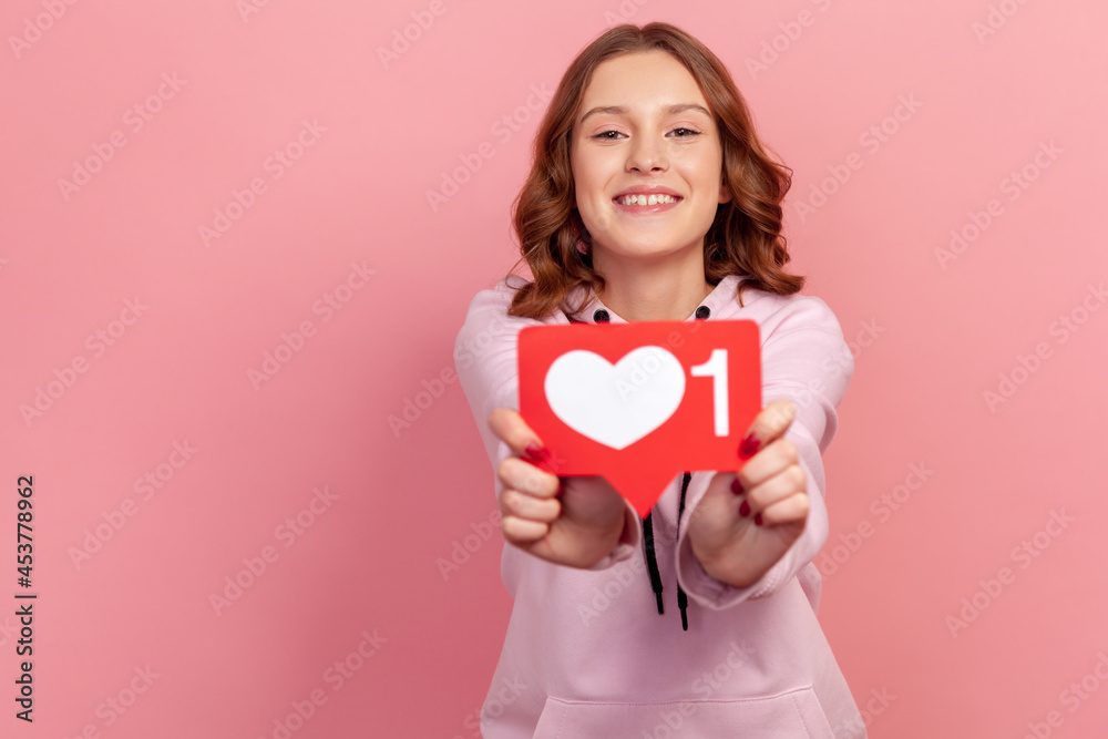 Portrait of cheerful smiling teenage girl showing heart icon at camera, recommending to follow, like me sign. Indoor studio shot isolated on pink background Portrait of cheerful smiling teenage girl showing heart icon at camera, recommending to follow, like me sign. Indoor studio shot isolated on pink background