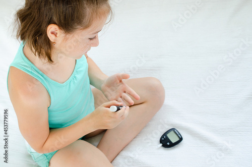 Little girl checking blood sugar level using lancelet and glucometer at home.