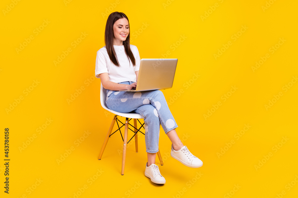 Full body profile side photo of young woman happy smile sit chair work laptop programmer isolated over yellow color background Full body profile side photo of young woman happy smile sit chair work laptop programmer isolated over yellow color background