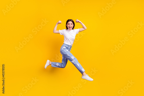 Full length profile side photo of young girl happy positive smile jump up go run show muscles isolated over yellow color background