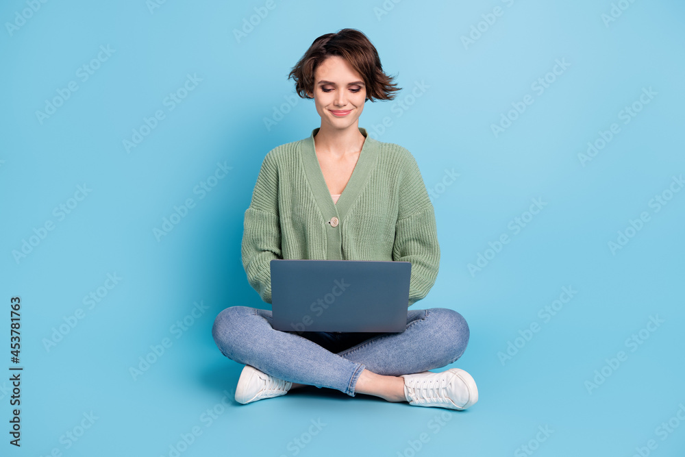 Full length photo of charming cute young lady wear green cardigan sitting floor typing modern device isolated blue color background Full length photo of charming cute young lady wear green cardigan sitting floor typing modern device isolated blue color background