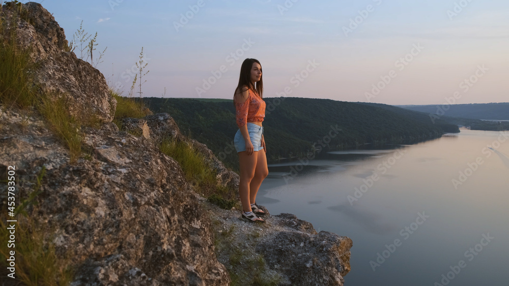The young woman stands on rocky mountain on beautiful river background