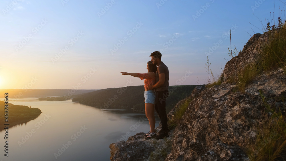 Obraz premium The young couple standing on rocky mountain above the beautiful river