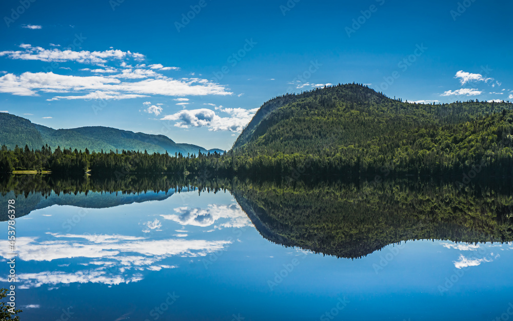 Reflection of the mountains and the blue sky in the quiet waters of Lake Resimond, in Saguenay (Quebec, Canada)