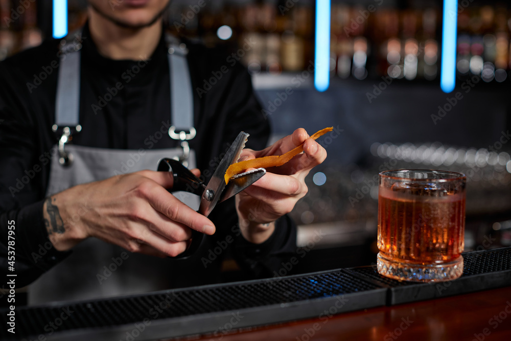 bartender makes a cocktail in a glass with orange peel