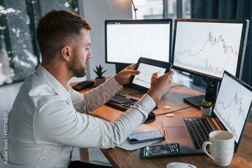 Looking at information. Young businessman in formal clothes is in office with multiple screens photo