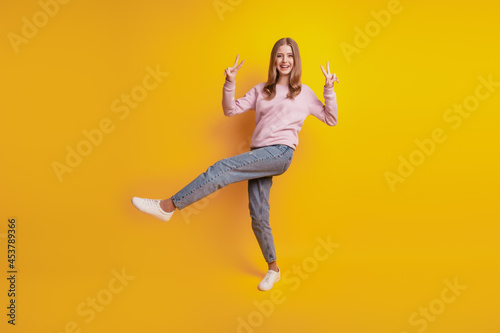 Photo of friendly cheerful girl stand one leg show v-signs on yellow background