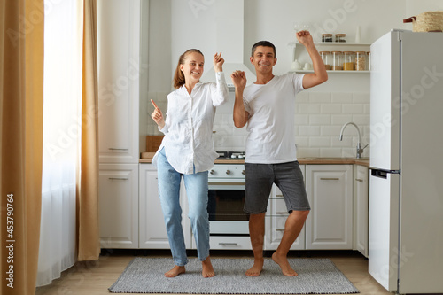 Slika na platnu Indoor shot of happy positive husband and wife dancing, having fun together in kitchen, celebrating relocation, being in good mood, expressing happiness