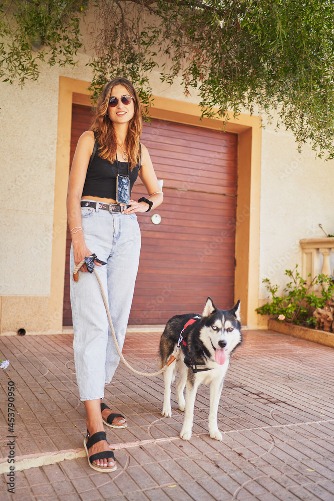 Young stylish woman stands looking at camera with her siberian husky in city