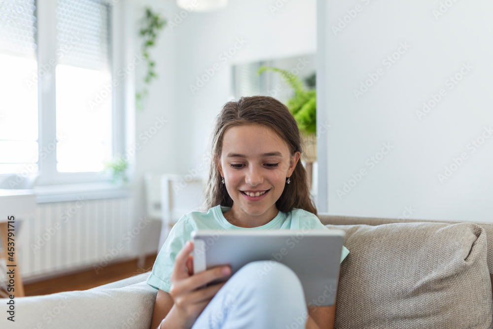cute little happy girl smile sitting down on sofa using looking digital tablet pad in the living room at home. family activity concept. cute little happy girl smile sitting down on sofa using looking digital tablet pad in the living room at home. family activity concept.