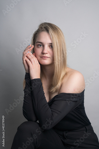 Girl, blonde, shoulder-length hair. Posing in the studio on a light background. Black clothes. Spring summer type. Baby face.