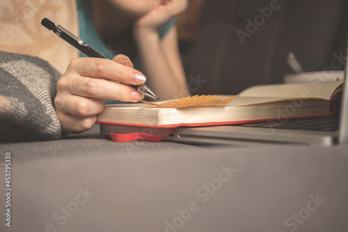 Dreamy girl write a diary at home in autumn holidays sitting on sofa with warm plaid. hand with pencil and autumn leaves on book