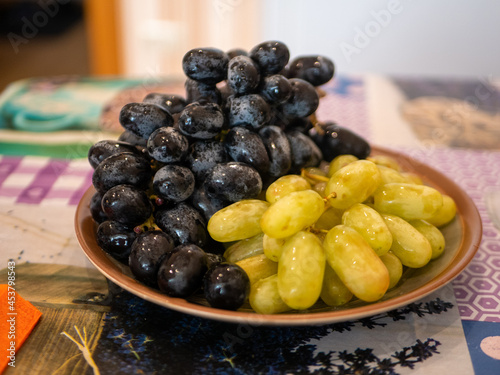 Bunches of grapes of two varieties, black and white, lie on a plate. Close-up