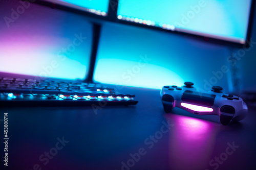 Fototapeta Naklejka Na Ścianę i Meble -  Low angle view of backlighted keyboard and game controller on table. Light blue illuminated wall in background.