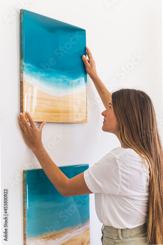 Female artist hanging a resin painting on a white wall