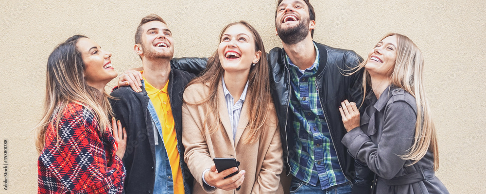 Group of friends standing by the wall background and enjoying each other-  Teenagers using smartphone and smiling while trying to take a selfie- Technology concept