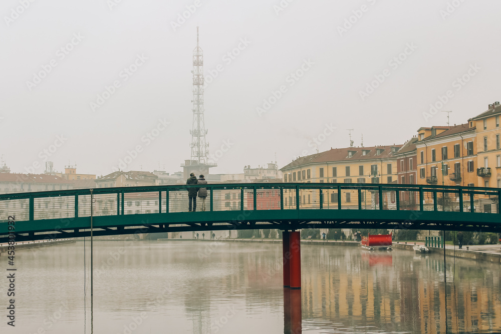 Unrecognisable couple standing on Alexander Langer bridge, Darsena waterfront on foggy winter morning, Milano city, Navigli district. Tourism destination concept