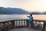 A woman in a blue dress looks at Lake Como and waves her hand. Photo