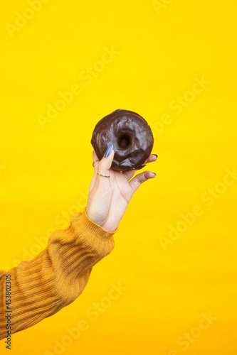 Fototapeta Naklejka Na Ścianę i Meble -  Woman hand holding a chocolate donut against a yellow background