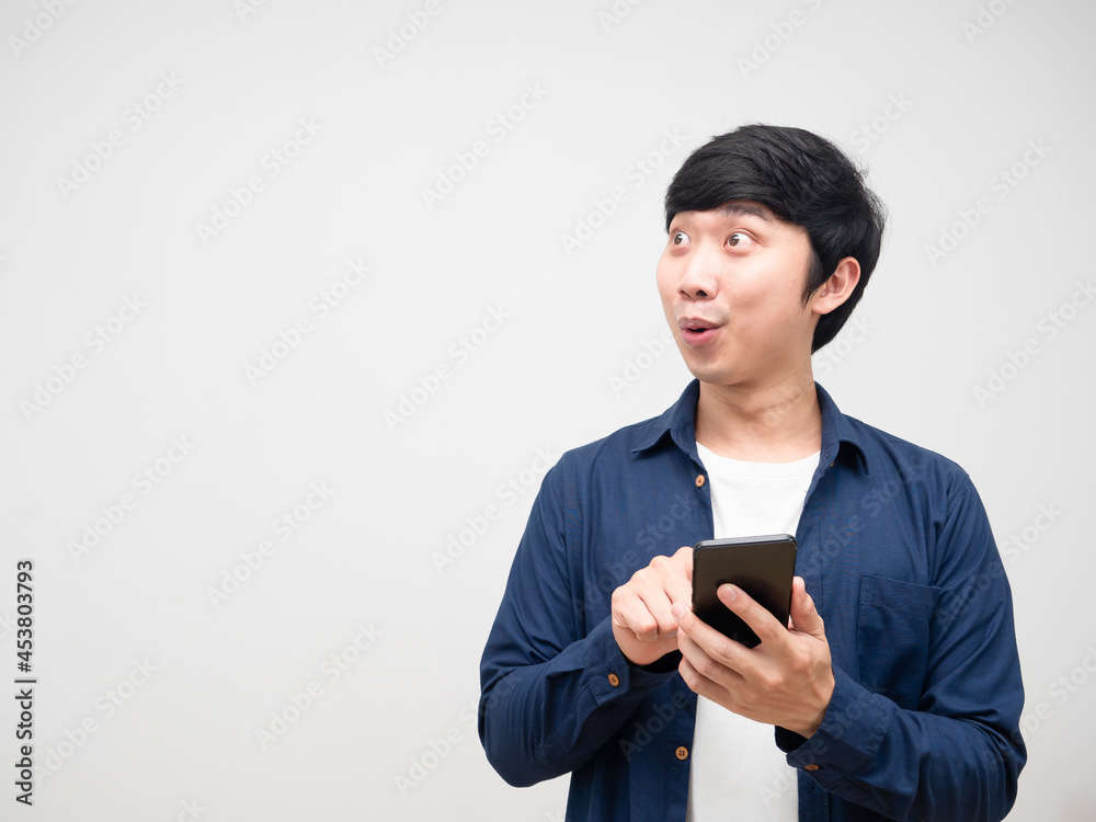 Asian young man holding and press mobile phone in his hand feeling excited and lookign at copy space white isolated Asian young man holding and press mobile phone in his hand feeling excited and lookign at copy space white isolated