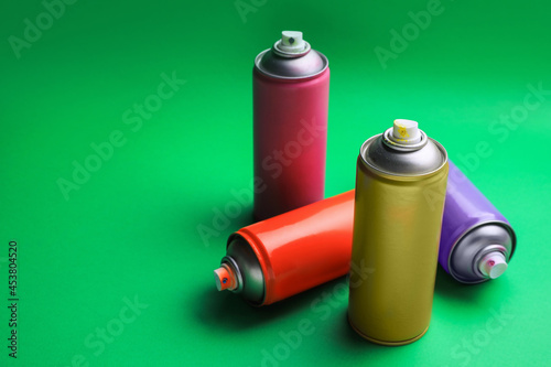 Cans of different graffiti spray paints on green background, space for text