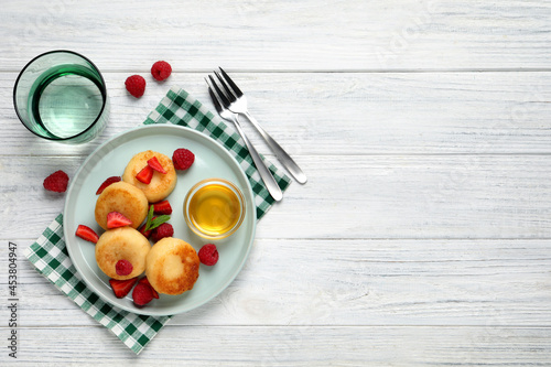 Delicious cottage cheese pancakes with fresh berries and honey on white wooden table, flat lay. Space for text